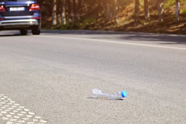 Boş bir plastik su şişesi yoldan geçen bir arabanın arka planına atıldı. Ekoloji ve temiz çevre sorunları.