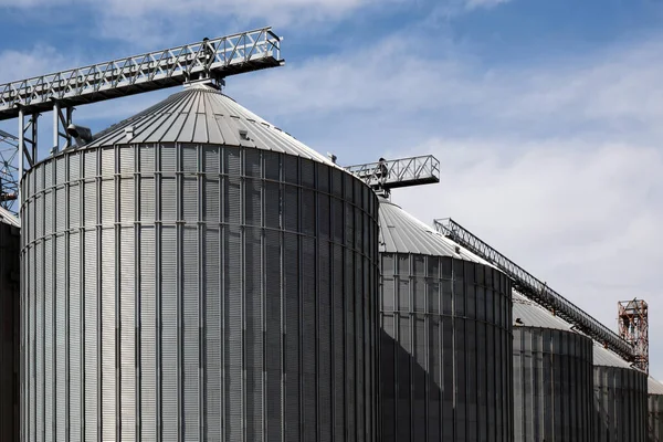 Steel grain storage silos with a conical bottom can be used for various purposes. Industrial facilities of feed and flour mills. Against the backdrop of a beautiful sky with clouds.