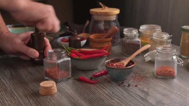 一个男人在家里用手工研磨机准备调味品 在一张漂亮的木制桌子上的玻璃瓶中 有大量的香料 辣椒和香料 全景运动 — 图库视频影像