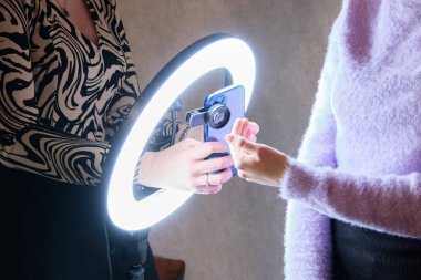 Manikürcü, tamamlanmış bir işi halkalı lamba kullanarak akıllı bir telefonla fotoğraflıyor..