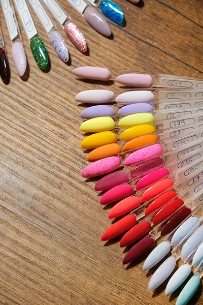 Vertical image of a palette closeup with samples of color and texture of nails for manicure. On a wooden table. Preparation for the beginning of the manicure procedure.
