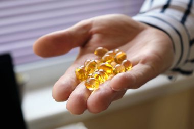 Elinde tıbbi haplar, yağ asitleri ve avucunda omega-3 vitaminleri olan bir adamın yakın çekimi. Sarı şeffaf renkli tıbbi kapsüller. Seçici odak.