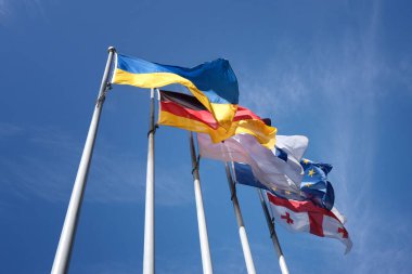 Çelik bir bayrak direğine asılmış birkaç ulusal bayrak rüzgarda dalgalanıyor. Ukrayna, Almanya, Avrupa Birliği, Gürcistan.