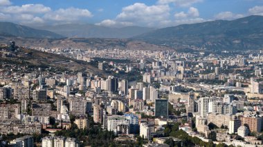 Dağların arkasında yüksek binaları olan büyük, modern bir şehrin havadan görünüşü..