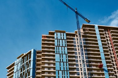 Yeni bir konut inşaatı için en alt kattan görüntü. Evin ön cephesi ve mavi gökyüzüne karşı yüksek bir vinç..