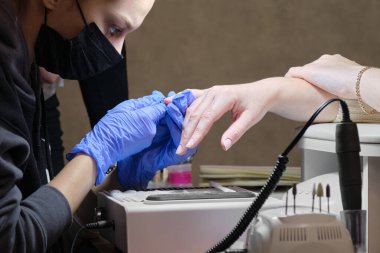 Manikür ustası kuaförde maske takıyor. Makasla tırnak içi çivileri işleniyor.