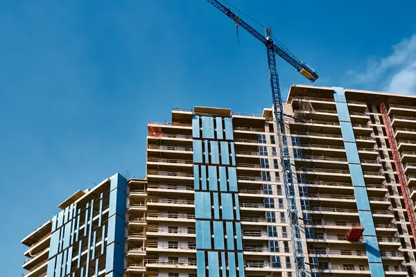 Yeni bir konut inşaatı için en alt kattan görüntü. Evin ön cephesi ve mavi gökyüzüne karşı yüksek bir vinç..