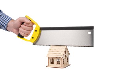 Bir adamın eli ahşap işçiliği için testereyi tutuyor ve tahta bir oyuncak evi kesiyor. Kavramsal görüntü. Beyaz arkaplanda izole.