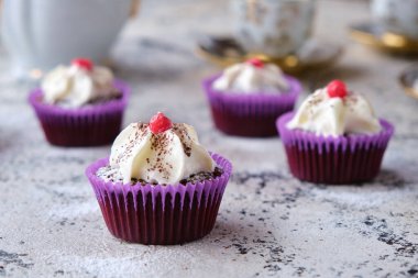 Bir çay takımının arka planında krema ve kızılcıklarla süslenmiş birkaç koyu çikolatalı kek..