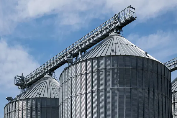 Steel grain storage silos with a conical bottom can be used for various purposes. Industrial facilities of feed and flour mills. Against the backdrop of a beautiful sky with clouds.