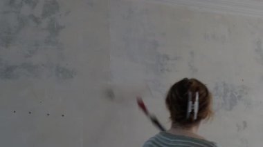 Genç kadın tamirci bir silindir kullanarak duvarı beyaz boyayla boyuyor. Dairede ya da ofiste tamir et..