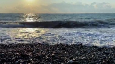 Deniz kıyısında güzel bir gün batımı. Büyük dalgalar kayalık kıyıya çarpar. Güneş ufuktan batıyor..