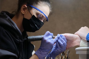 Manikür ustası kuaförde maske ve gözlük takıyor. Makine işleme kesicisi.