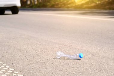 Boş bir plastik su şişesi yoldan geçen bir arabanın arka planına atıldı. Ekoloji ve temiz çevre sorunları.