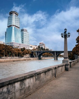 Modern gökdelenlerin arka planına karşı eski bir nehir setinin dikey görüntüsü ve bulutlu güzel bir gökyüzü..