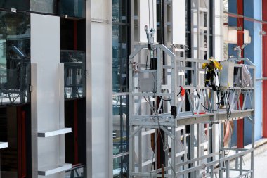 İşçiler için modern metal platformu binanın ön cephesinde yüksek irtifa çalışması yapıyor. Yeni merkezin yeni bir ev veya ofis inşaatı.