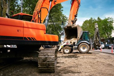 Şehirdeki su ve kanalizasyon sisteminin yerini kamu hizmetleri işçileri alıyor. Yoldaki kazıcıda çalışıyor..
