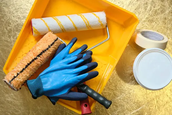 Top view tool for repairing or painting walls and ceilings indoors. Roller, yellow plastic tray, protective gloves, paint.