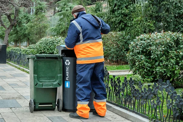 Üniformalı bir kamu görevlisi, şehir caddesindeki bir çöpten çöp topluyor..