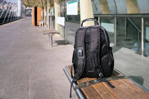 A lost or forgotten backpack on a bench on an open platform of a city metro or train.
