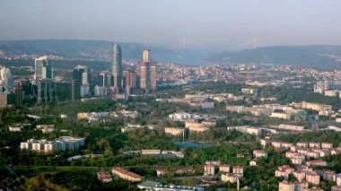 Gökdelenleri, parkları ve deniz kıyıları olan modern bir şehre. Bulutlu bir günbatımı gökyüzünün arka planında. Bir gökdelenin penceresinden görüntüle.
