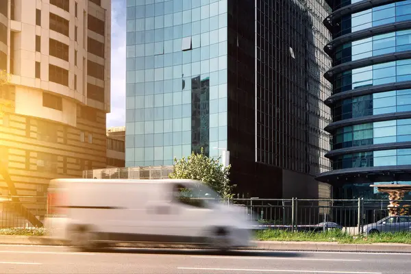 A car with a delivery service van drives quickly along the road in the city against the backdrop of skyscrapers. Blurred motion.