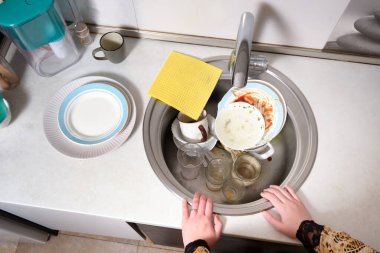 Bir kadın, akşam yemeğinden sonra evde kirli bulaşıklarla mutfak lavabosunun önünde duruyor. Rutin ev işlerini yapmakta isteksizsin..