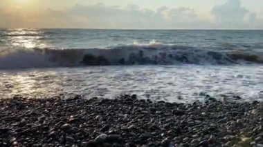 Deniz kıyısında güzel bir gün batımı. Büyük dalgalar kayalık kıyıya çarpar. Güneş ufuktan batıyor..