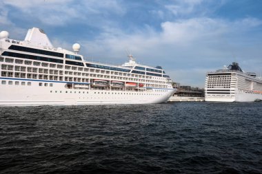 İki büyük deniz yolcu gemisi şehrin arka planına karşı iskelede duruyor ve bulutlu güzel bir gökyüzü. Popüler deniz seyahatleri.