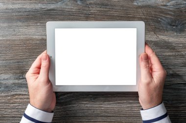 Orta yaşlı bir adam elinde bir tablet tutuyor. Güzel ahşap bir masanın arka planında. Tasarımcı için şablon.