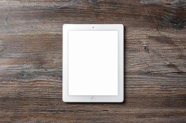 Güzel ahşap bir masanın üzerinde duran beyaz tabletin üst görüntüsü. Tasarım şablonu.