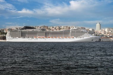 Arka planda şehir olan büyük bir yolcu gemisi rıhtımda duruyor. Popüler deniz seyahatleri.
