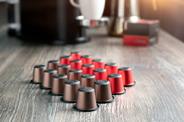 There are many colorful capsules for the coffee machine on a beautiful wooden table. In a home kitchen against the background of a coffee machine and cups.