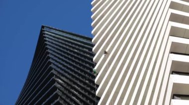 Bir temizlik şirketi bir gökdelende iş yapıyor. Çalışanlar binanın pencerelerini ve cephelerini temizliyor. İki modern yüksek katlı binanın güzel geometrik arka planı yan yana.