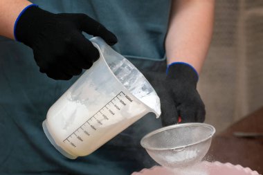 Dekoratif mum ya da sabun malzemesi yapmak için malzemeleri karıştıran koruyucu eldivenli bir kadının elini yakın plan çek. Evde pratik yapmak için iyi bir hobi..