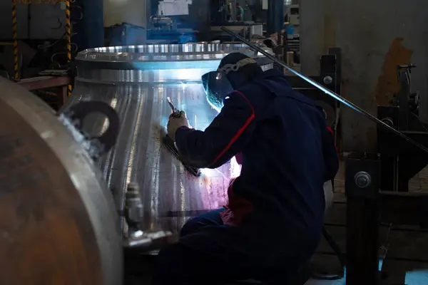A welder works with a large metal structure at a mechanical engineering plant. Manufacturing of large units for heavy industry.