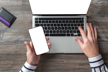 Orta yaşlı bir adam elinde bir akıllı telefon tutuyor ve bir dizüstü bilgisayarla çalışıyor. İnternet üzerinden satın alma ve hizmetler için ödeme.