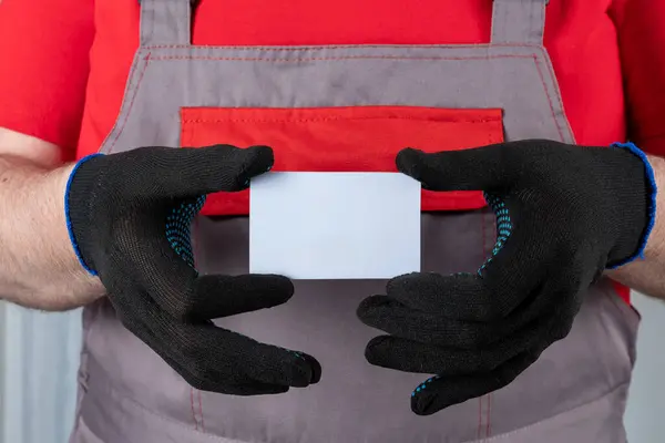 A man in work clothes and gloves holds a plastic card in his hands. Template for advertisements.