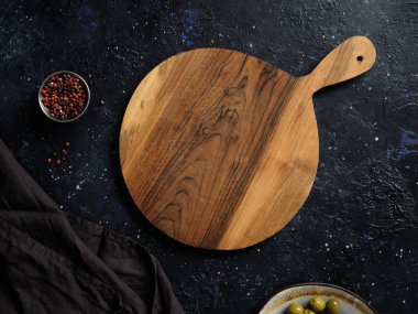Top view of empty round wooden cutting board with handle, red pepper and green olives on abstract dark background. Template for restaurant or cafe menu design. clipart