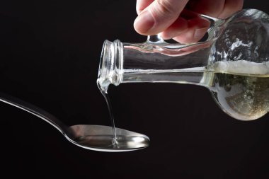 Aşçı bir kaşığa ayçiçeği yağı ve cam şişeler döker. Karanlık bir arka planda.