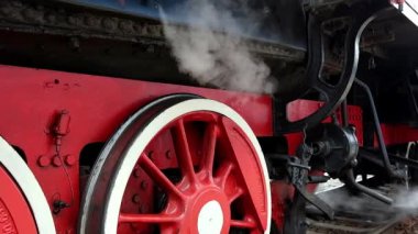 Tren istasyonundaki buharlı lokomotif tekerleklerinin yakın çekimi. Trenin arka planına karşı buhar esintisi. Çalışan tren 