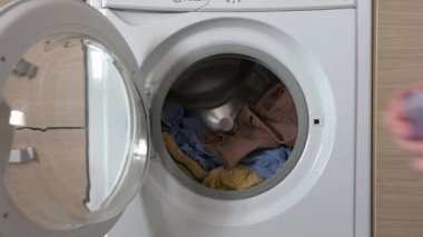 Bir adam çamaşır makinesinin variline çamaşır jeli döker. Renkli ve beyaz kıyafetler için modern temizlik ürünleri.