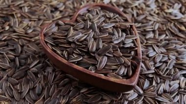 Çizgili ayçiçeği çekirdekli kalp şeklinde ahşap kase. Tohumların arka planına karşı. Seçici odaklanma. Resmi döndür. 