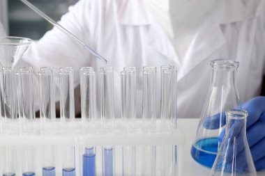Laboratuvardaki bir bilim adamı renkli bir sıvıyı test tüplerinde analiz etmek için pipet kullanıyor. Konsept: araştırma, biyokimya, doğa, ilaç.