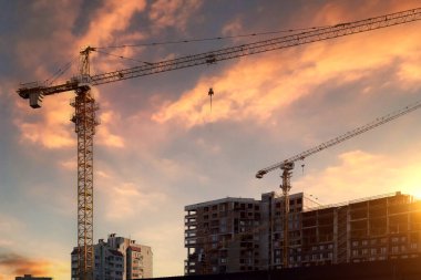 Yeni bir konut kompleksi inşaatı. Güzel bir günbatımı gökyüzünün arka planına karşı iki gökdelenli vinç.
