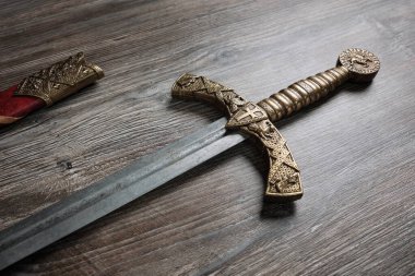 Bronz kabzalı ve kılıç kınlı güzel bir ortaçağ kılıcı ahşap bir masanın üzerinde yatıyor. Ortaçağ zanaatkarlarının maharetli işi..