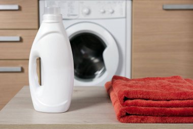 Çamaşır makinesinin içine sıvı çamaşır jeli katılmış yakın plan beyaz plastik şişe. Renkli kumaş için modern temizlik ürünleri.