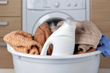 Kirli çamaşırlarla dolu bir sepetin ve plastik bir şişe sıvı jelin yakın çekimi. Renkli kumaşlar için modern temizlik ürünleri. Bir çamaşır makinesinin arka planında.