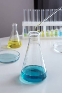 Diğer laboratuvar camlarının arka planına karşı kimyasal deneyler için cam şişelerin yakın plan görüntüleri. Seçici odak.