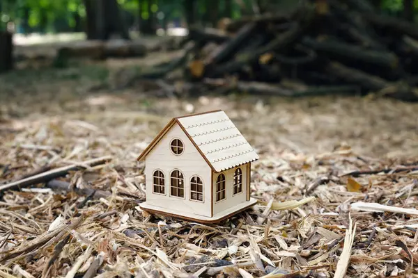 stock image Close-up a beautiful small wooden toy house against the backdrop of a cleared forest. The concept of building an eco-house and preserving environment.